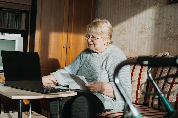 An older woman reviewing paperwork alongside her laptop at home, staying independent and connected with the right supports in place